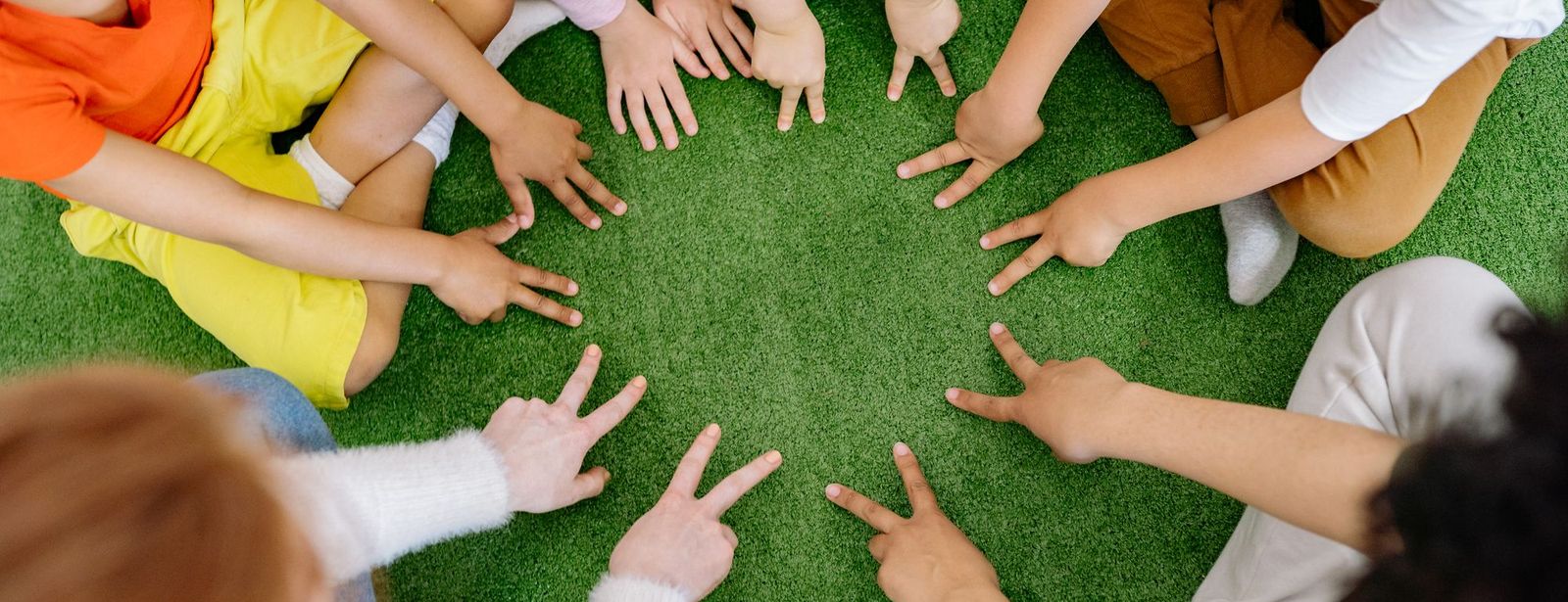 Kinderhände strecken sich in einem Kreis auf einer Wiese zusammen