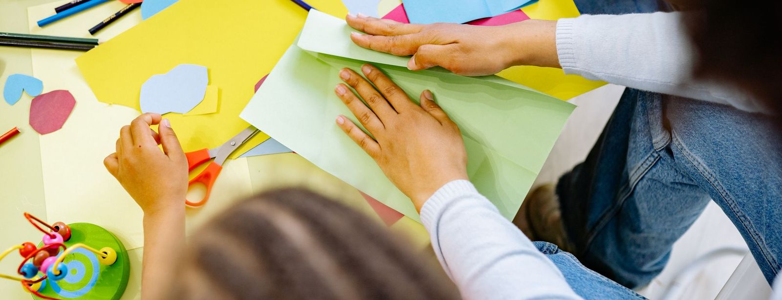 Kinderhände arbeiten an einem Basteltisch mit buntem Papier