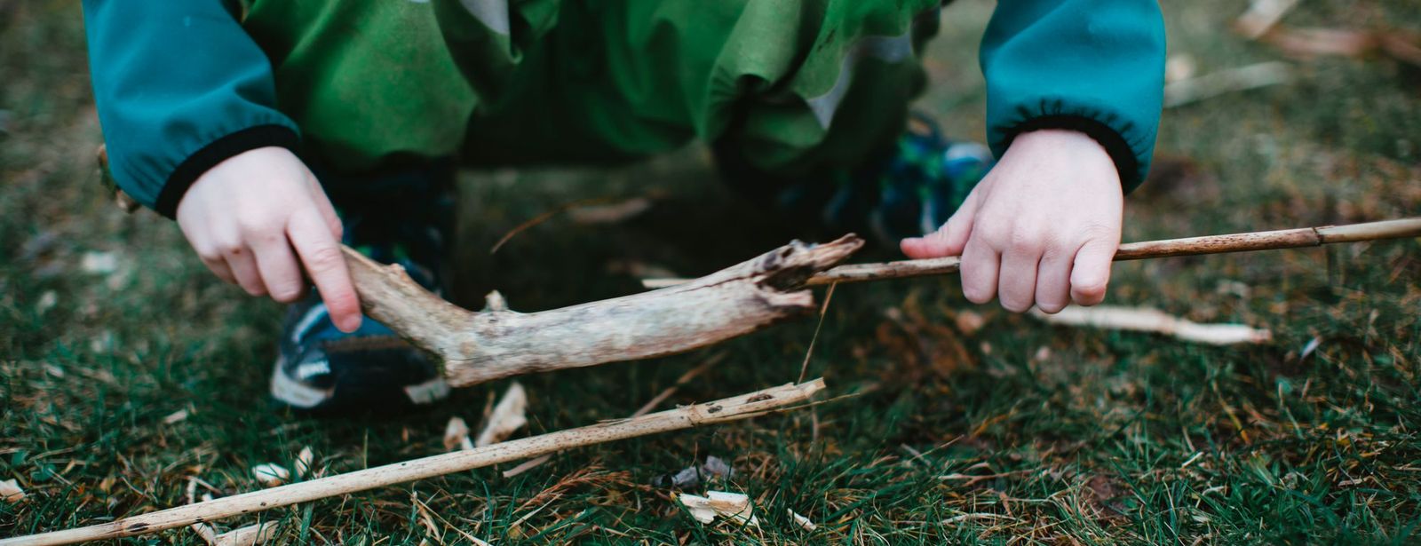 Kinderhände legen Äste und Zweige auf einer Wiese aus