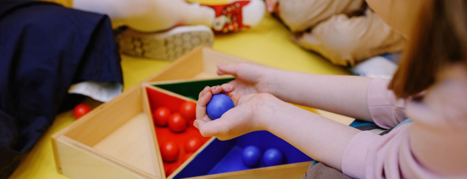 Kinderhände sortieren bunte Kugeln in ein Holzfach